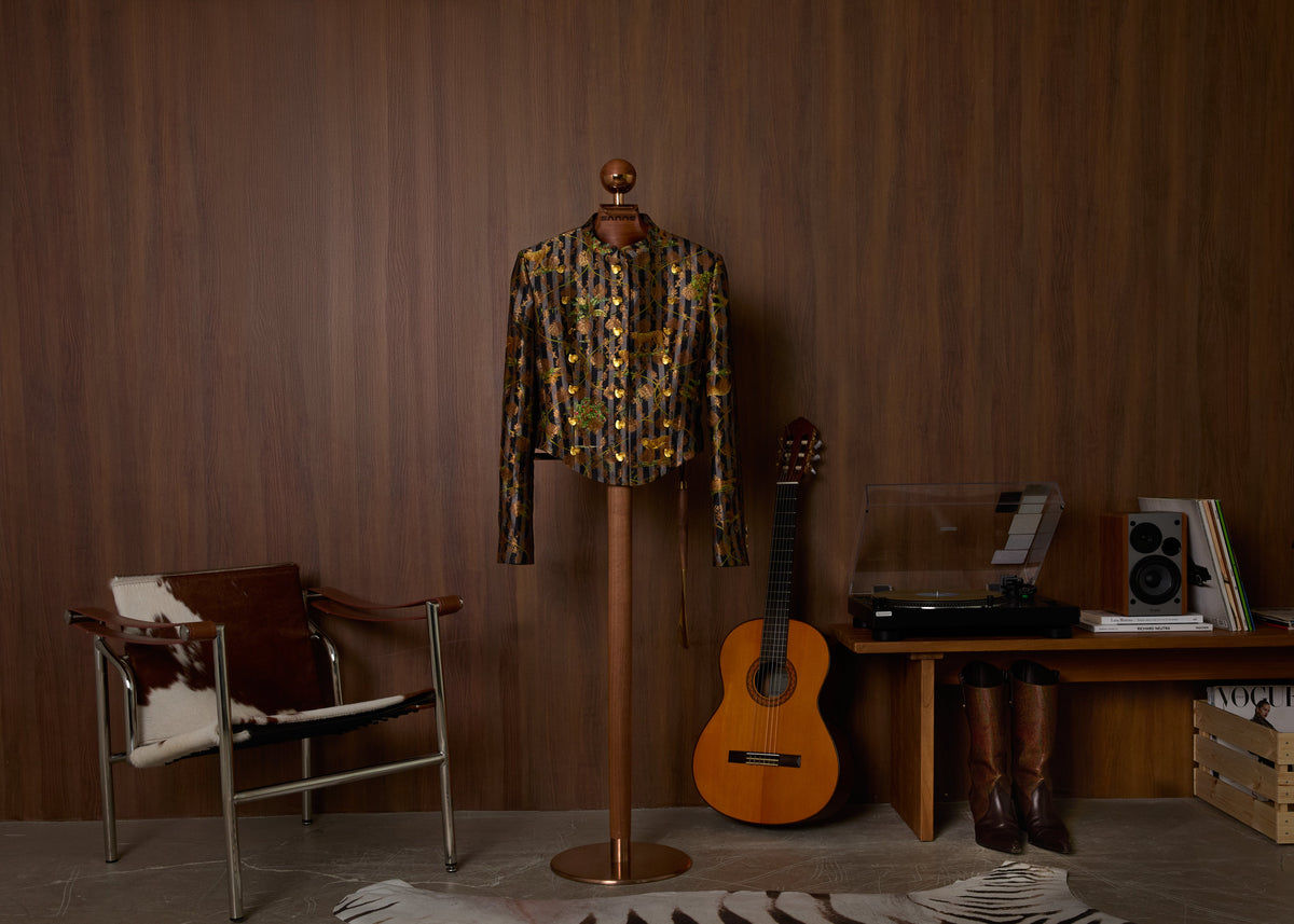 Sanne cropped brocade jacket with gold embroidery on a brass stand, beside a guitar and turntable.